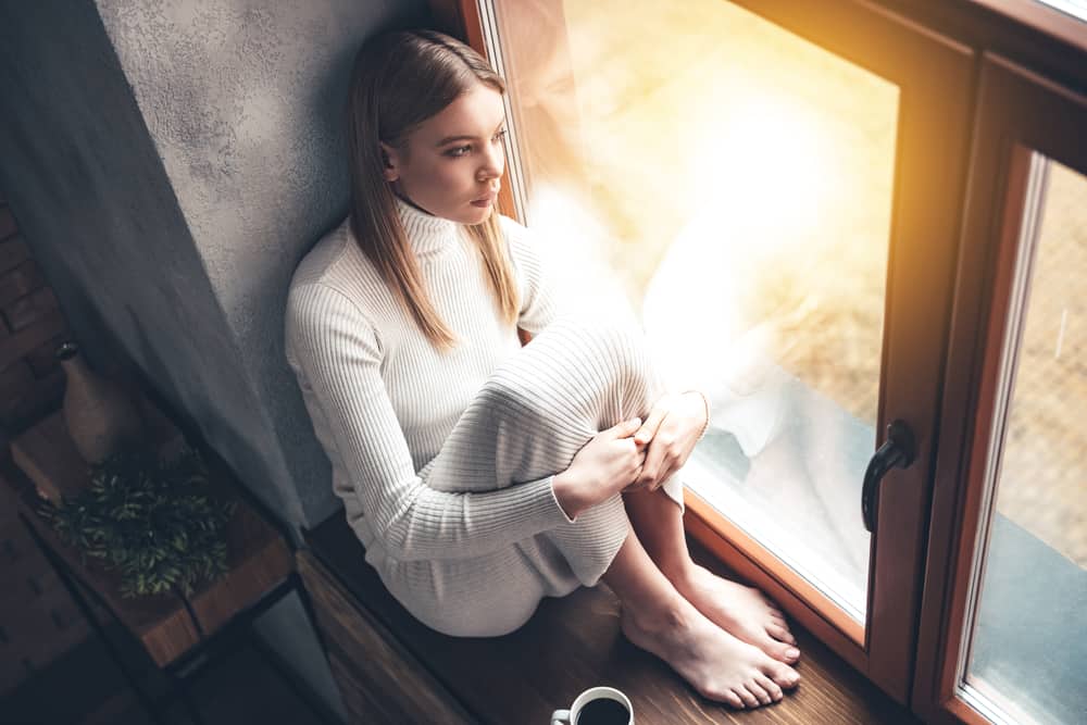 une femme imaginaire est assise près de la fenêtre avec une tasse de café et pense