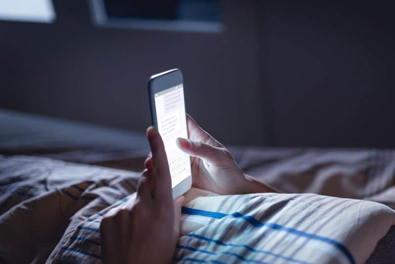 une femme le soir s'allonge sur une crête couverte et lit un sms