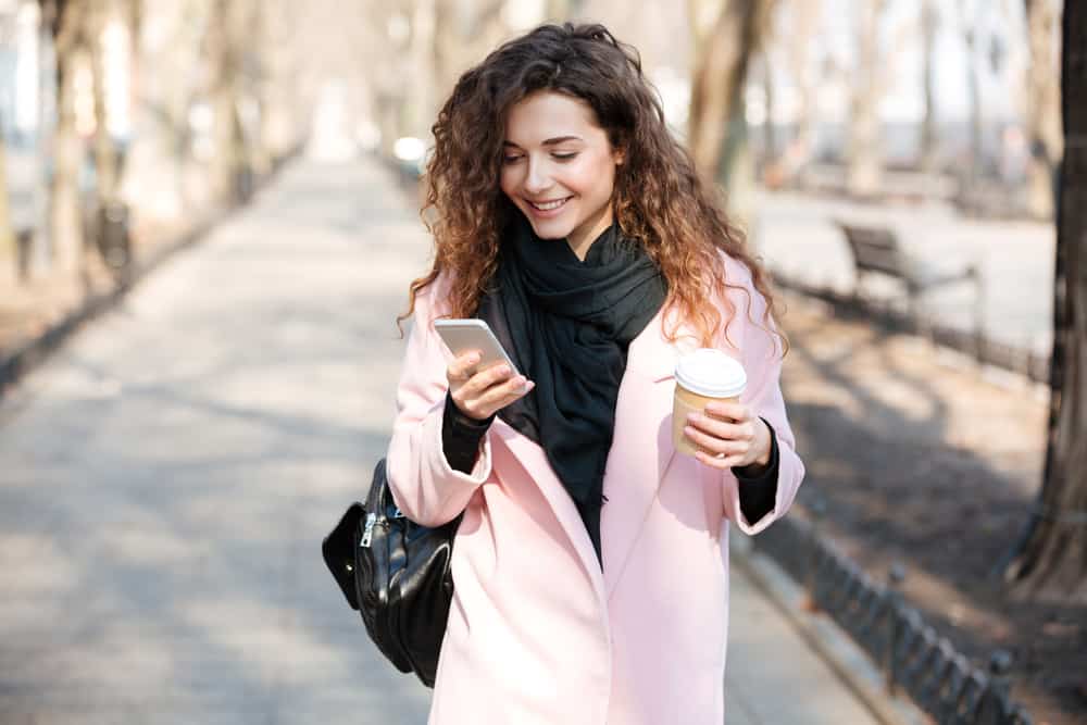une femme marche dans la rue en buvant du café et en appuyant sur un téléphone