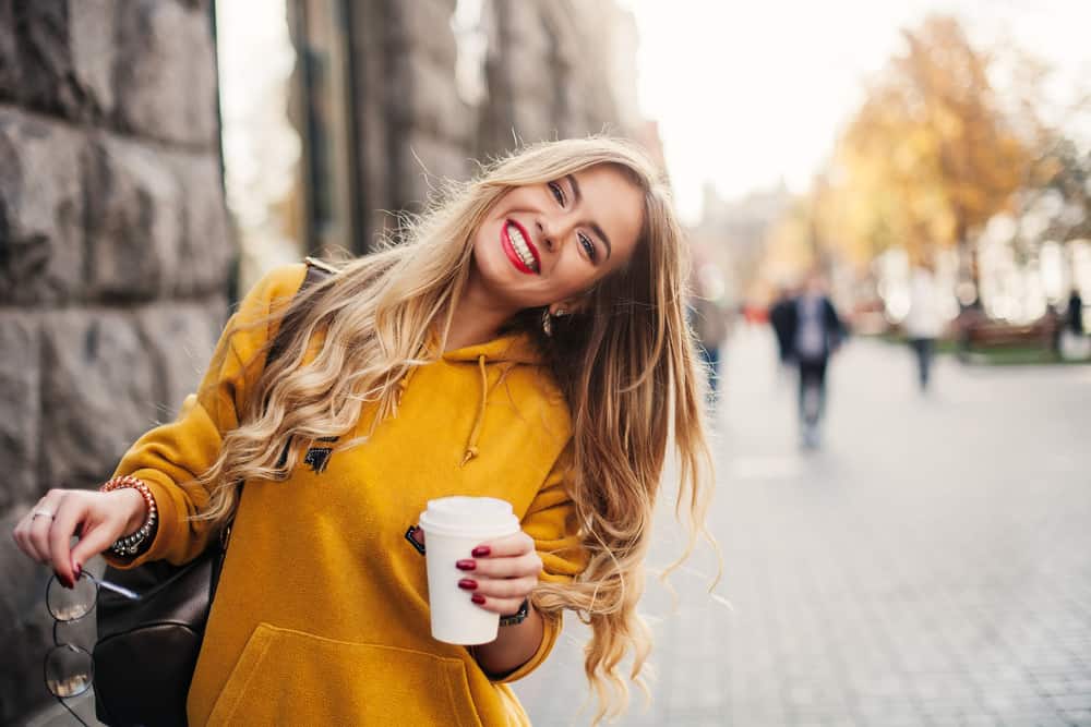 une femme marche dans la rue en riant avec du café à la main