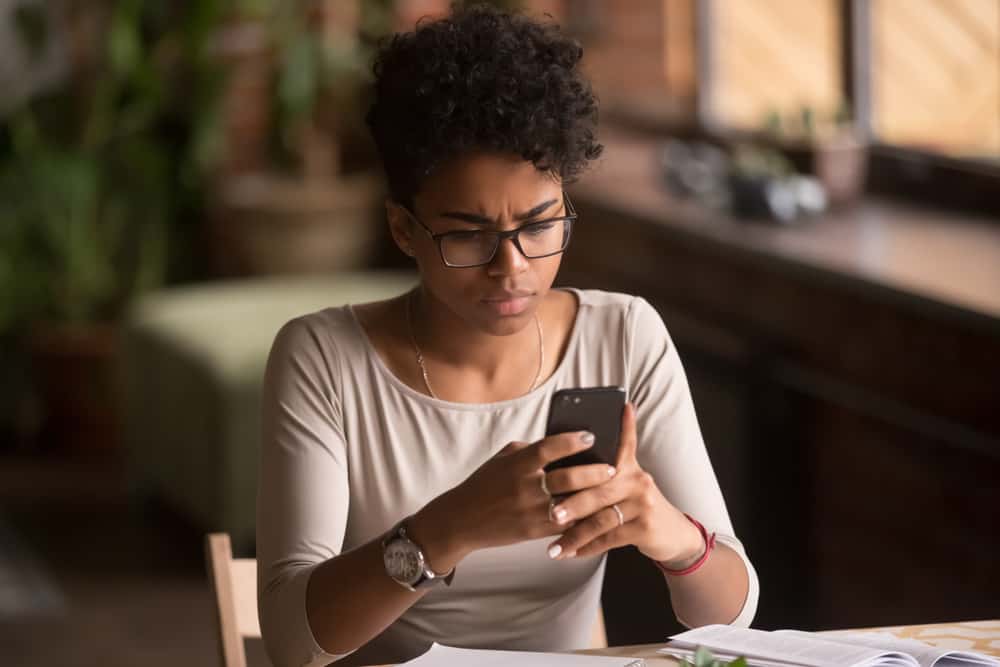 une femme noire confuse avec des lunettes écrit un sms