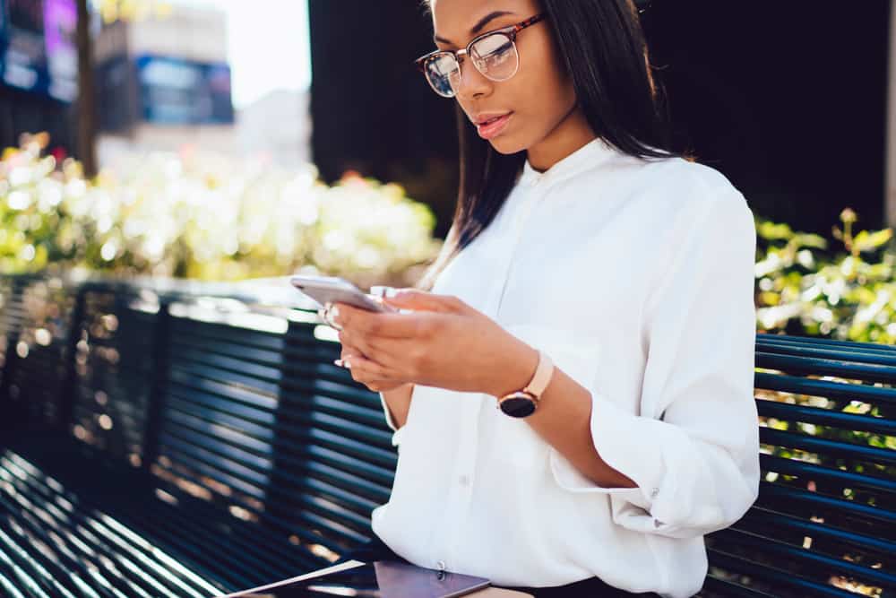 une femme noire sérieuse se tient dehors et envoie des SMS