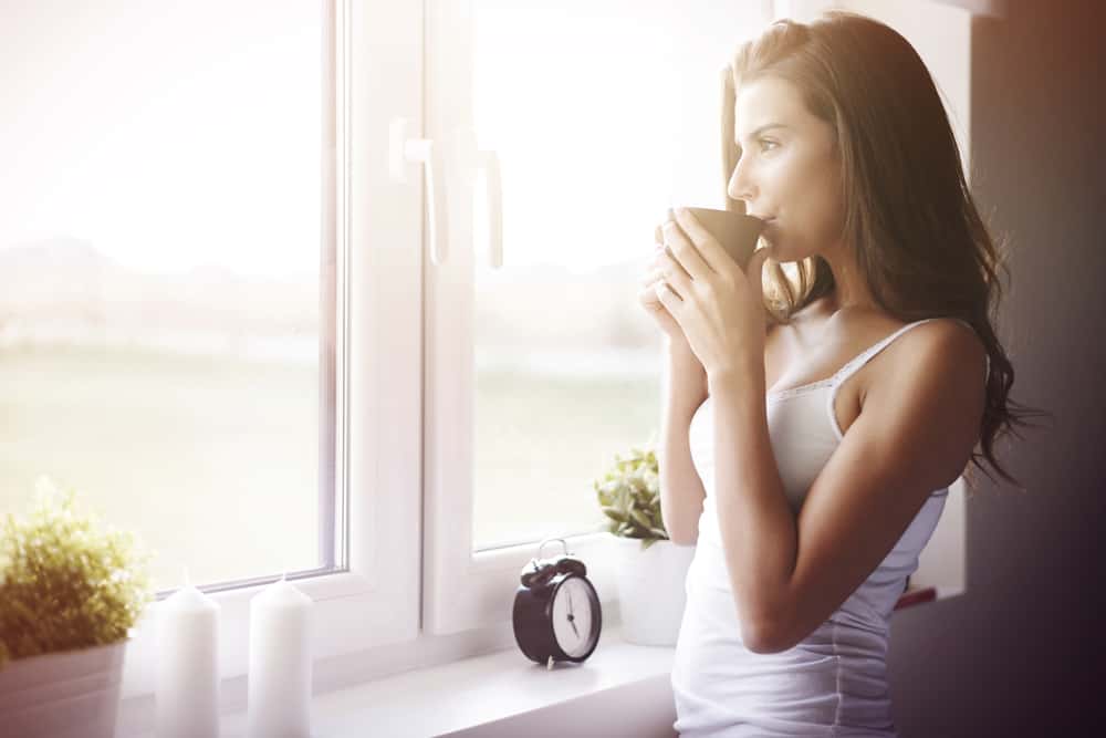 une femme par la fenêtre buvant le café du matin