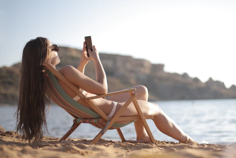 une femme prend un bain de soleil sur la plage et utilise un smartphone