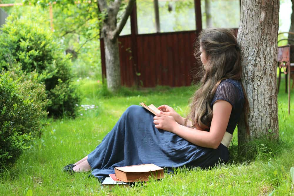 une femme près d'un arbre est assise et écrit une lettre