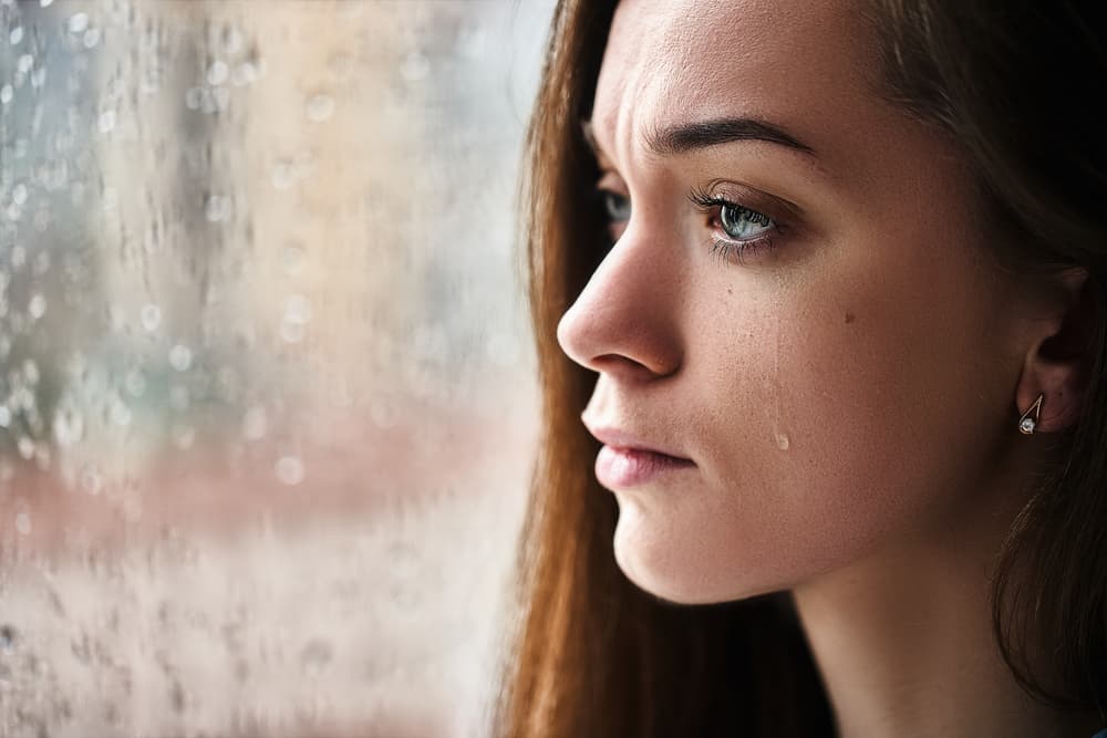 une femme se tient près de la fenêtre et pleure