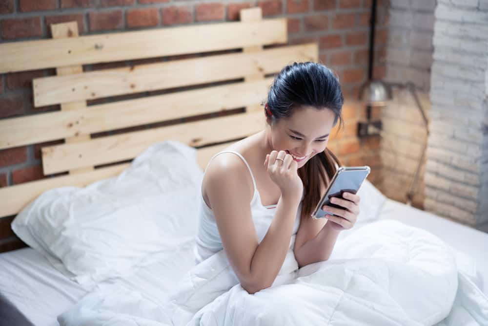 une femme souriante dans un lit utilise le téléphone
