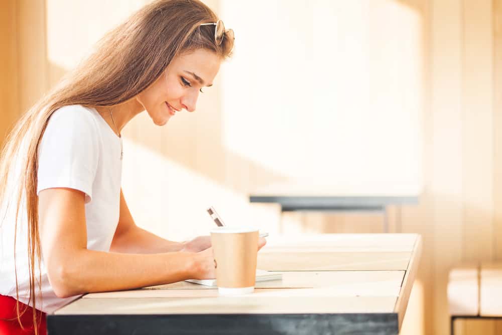 une femme souriante s'assied et écrit quelque chose