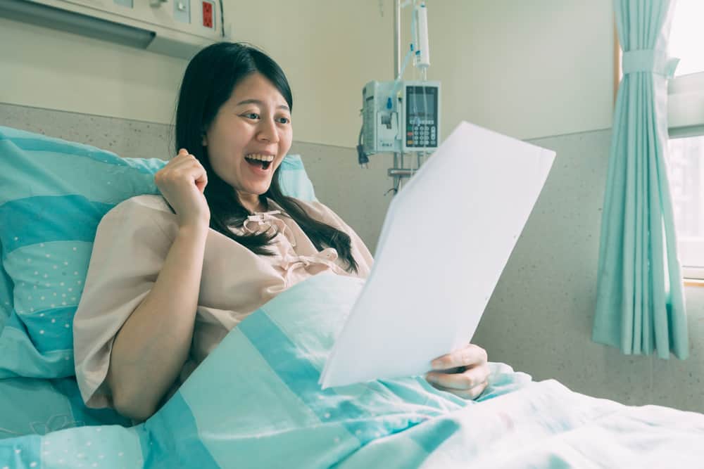 une femme souriante se trouve dans un lit d'hôpital et lit une lettre