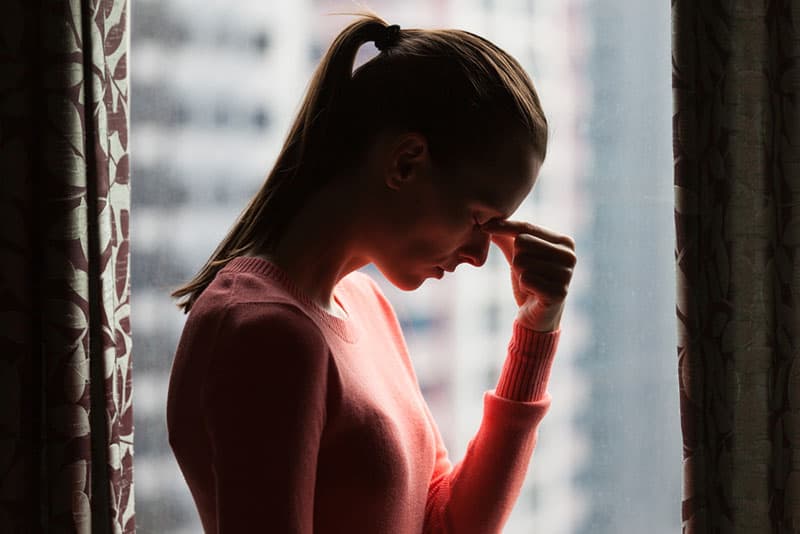 une femme stressée debout devant une fenêtre