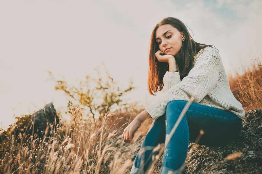 une femme triste est assise dans un champ de blé