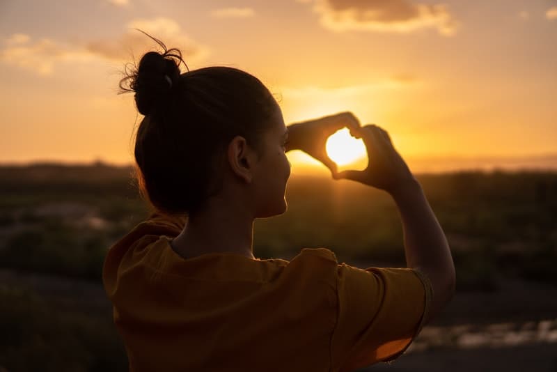 une fille au coucher du soleil avec ses mains lave une figure d'un coeur