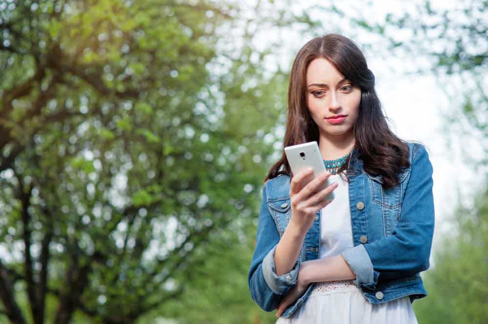 une fille dans une veste en jean se tient à l'extérieur et pense en regardant un smartphone