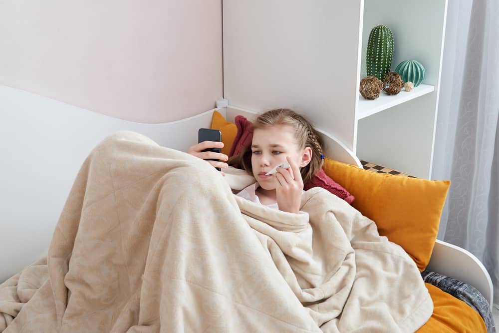 une fille malade se couche et utilise un smartphone