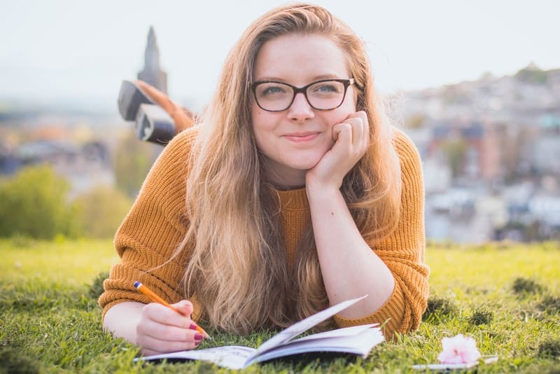 une fille souriante se trouve sur l'herbe et écrit