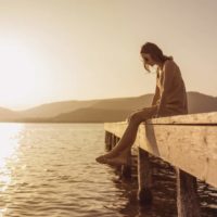 femme assise sur une jetée d'un lac et regardant en bas