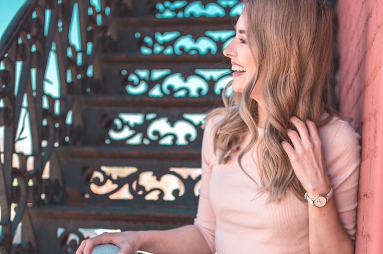 vue de côté d'une femme blonde souriante appuyée sur le mur