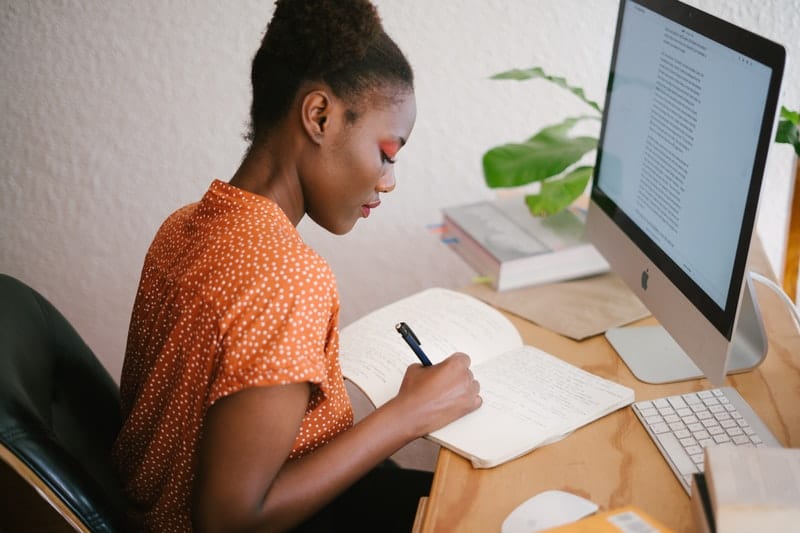 Une femme assise devant un ordinateur portable et écrit quelque chose sur un morceau de papier