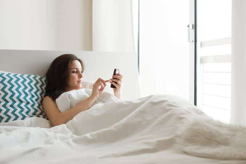 Une femme au lit vérifie les applications sociales avec son smartphone