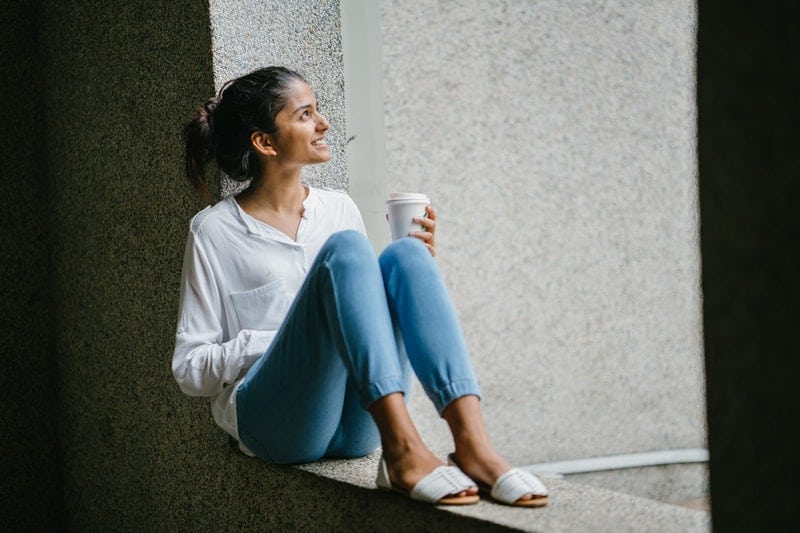 Une femme est assise sur un mur avec du café à la main et regarde le ciel