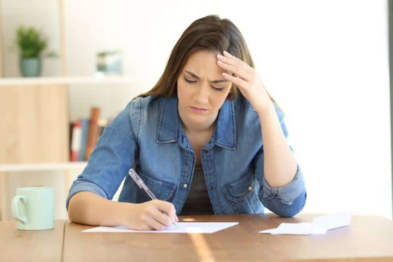Une femme malheureuse qui écrit sur du papier à la maison