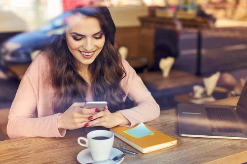 Une femme souriante tape sur son téléphone dans un café