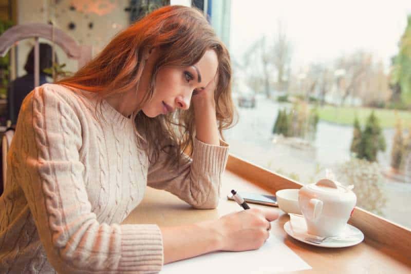 Une femme triste et dépressive écrit une lettre dans un café