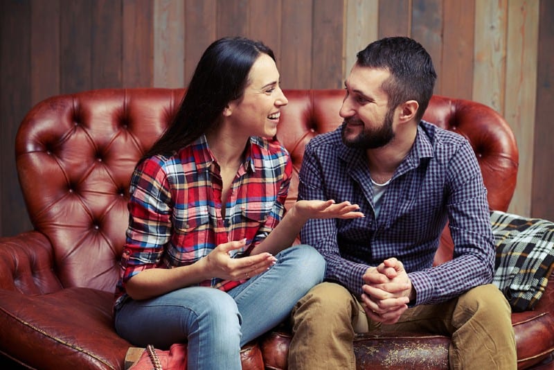 couple heureux parler assis côte à côte sur un canapé rouge