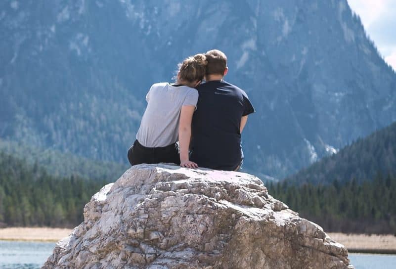 un homme et une femme assis sur une pierre embrassant