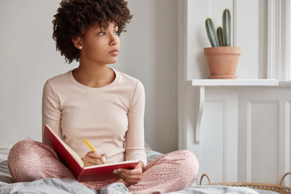 une femme aux cheveux crépus est assise et écrit