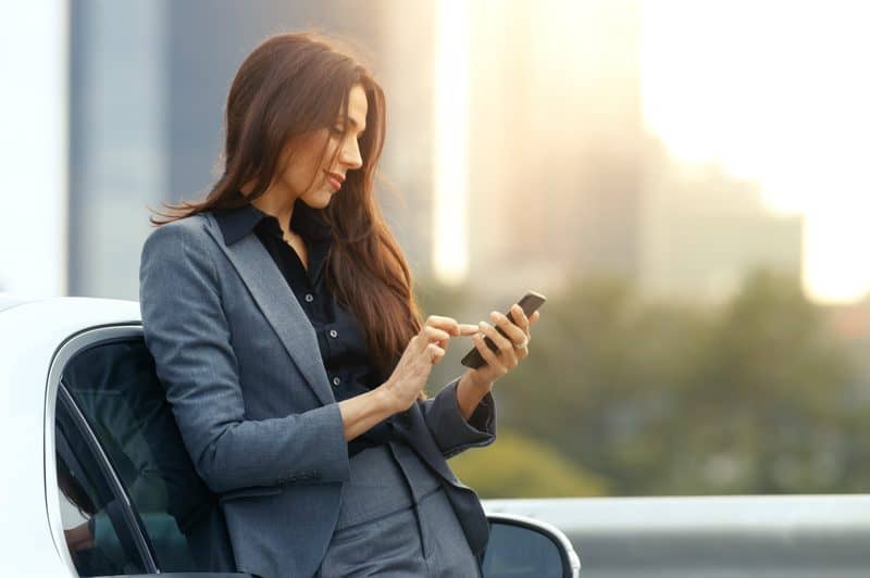 une femme avec un téléphone à la main appuyé contre une voiture