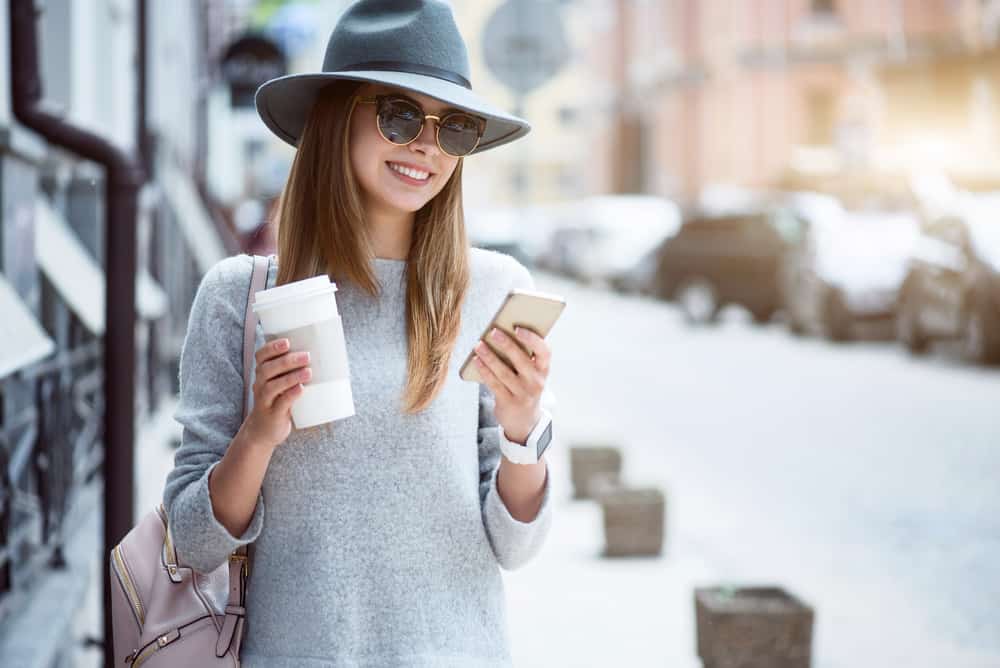une femme dans la rue est debout avec du café à la main et un téléphone