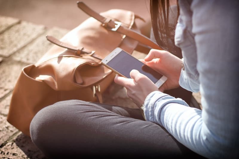 une femme est assise à côté d'une jetée avec un téléphone à la main