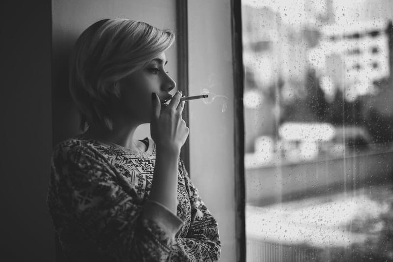 une femme se tient près de la fenêtre et fume