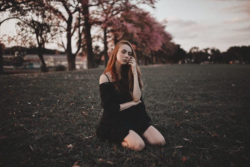 une jolie fille aux cheveux roux en robe noire courte est assise dans l'herbe