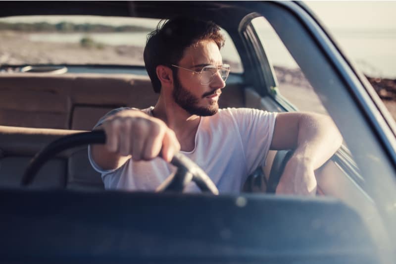 Bel homme barbu est assis dans sa voiture rétro verte