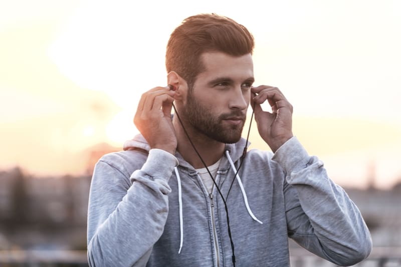 Confiant jeune homme mettant des écouteurs dans ses oreilles