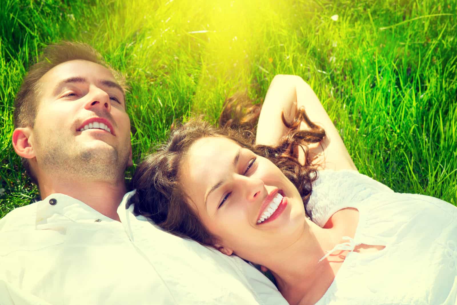 un homme et une femme s'allongent sur l'herbe et rient