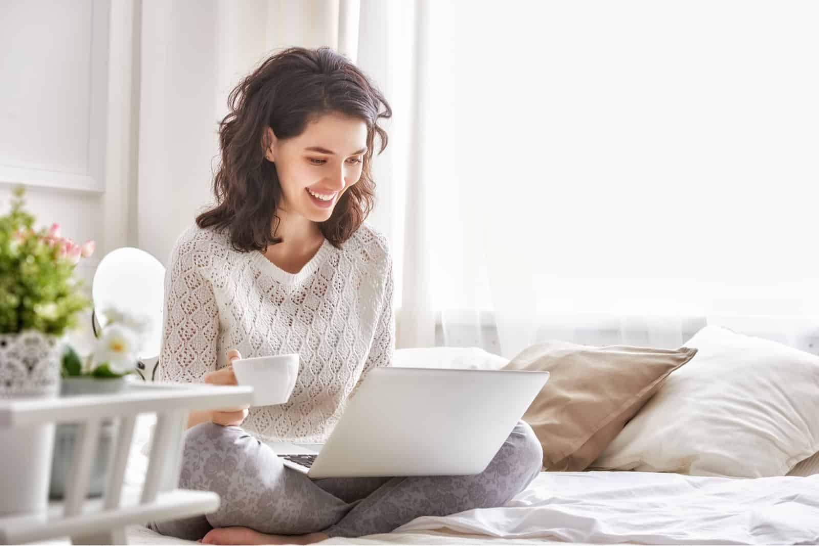 Une femme assise devant un ordinateur portable en riant et en buvant du café