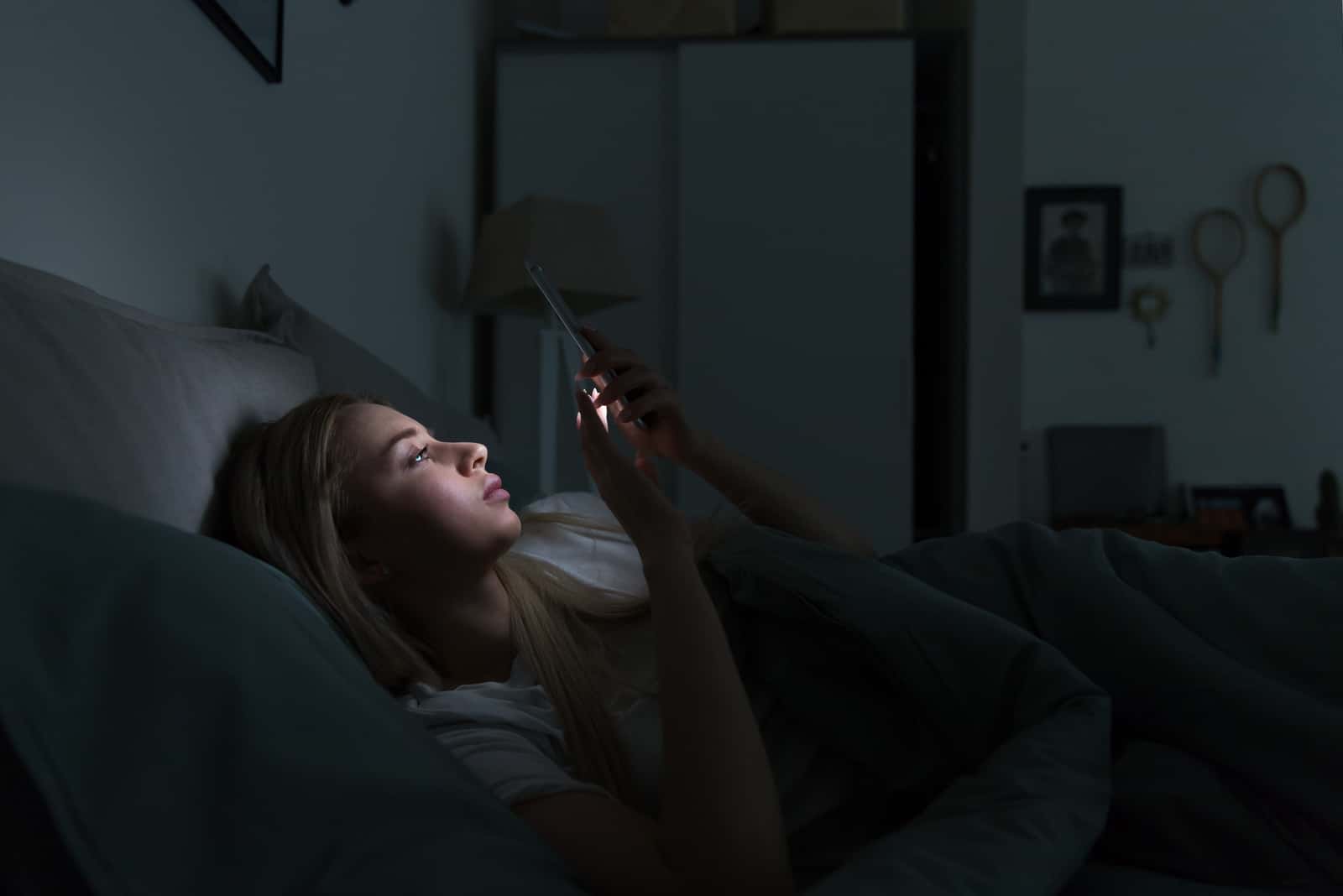 la femme est allongée dans son lit avec le téléphone à la main 