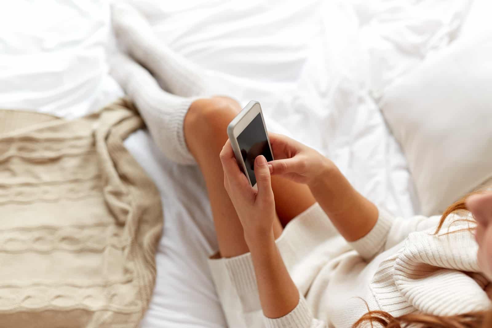 la femme est allongée dans son lit avec le téléphone à la main