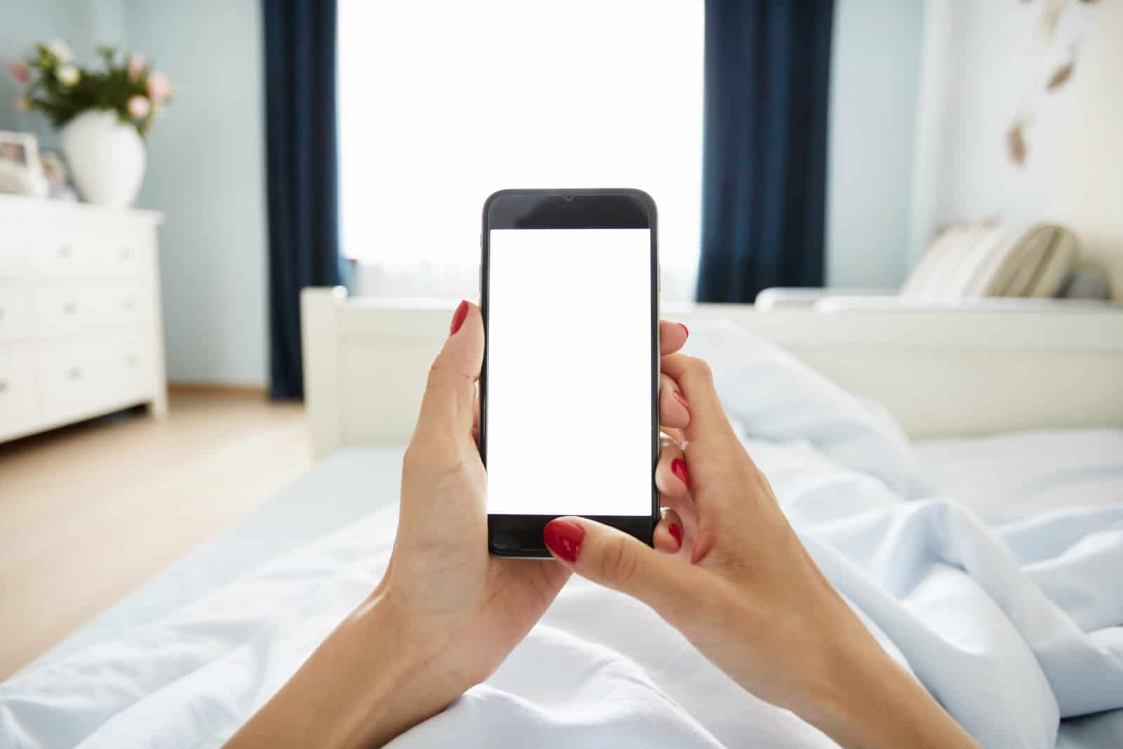 la femme est allongée dans son lit et tient un téléphone dans sa main