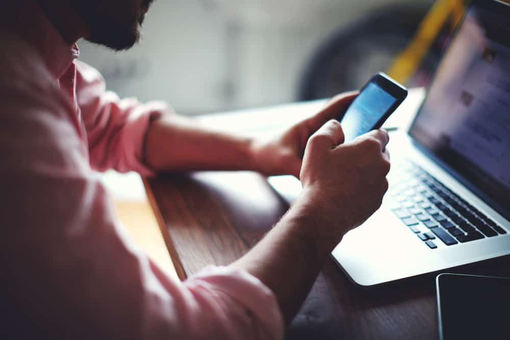 un homme est assis à côté d'un ordinateur portable et tient un téléphone dans sa main