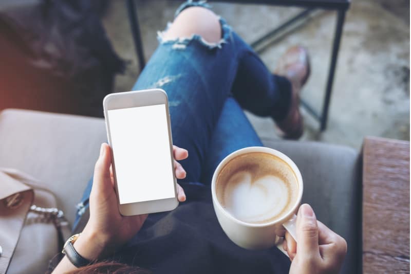 une femme assise tenant un téléphone et un café à la main