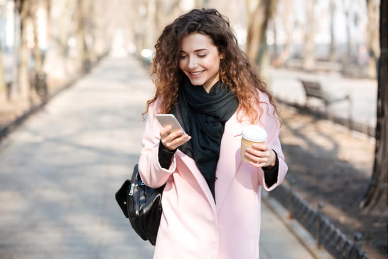 une femme debout dans la rue avec un téléphone à la main et un café