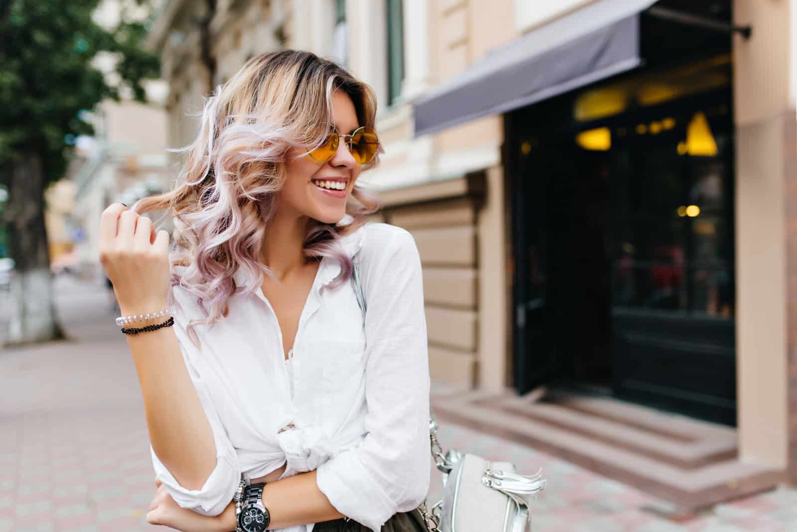 Jolie fille portant des lunettes de soleil et des bracelets jouant avec ses cheveux courts bouclés