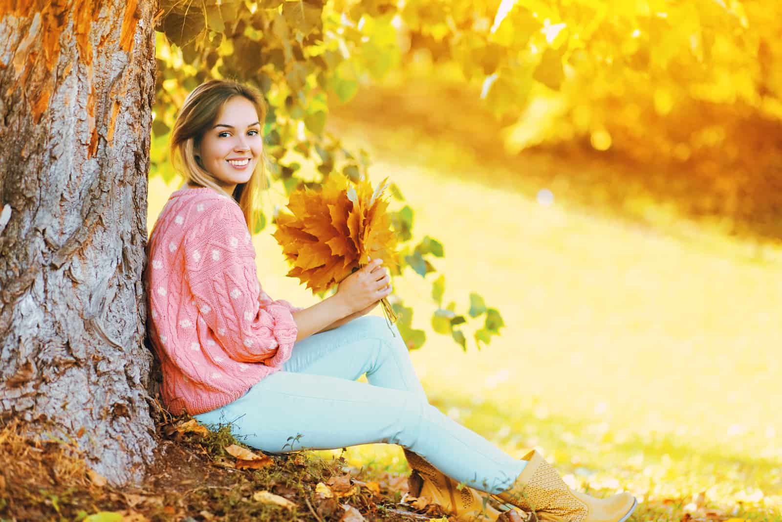 Une femme assise à côté d'un arbre tenant des feuilles dans sa main