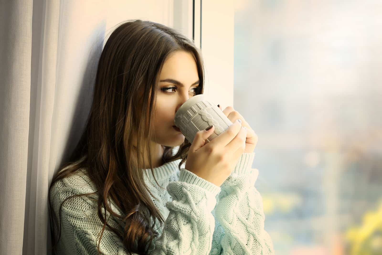 la femme est assise près de la fenêtre en train de boire du café
