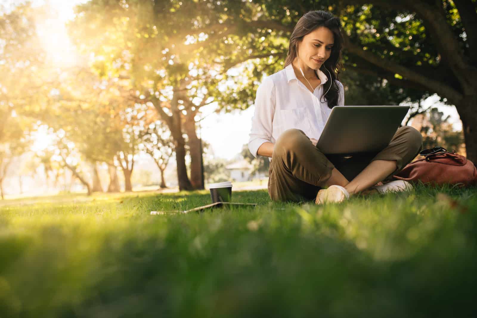 une femme assise sur l'herbe avec un ordinateur portable sur ses genoux