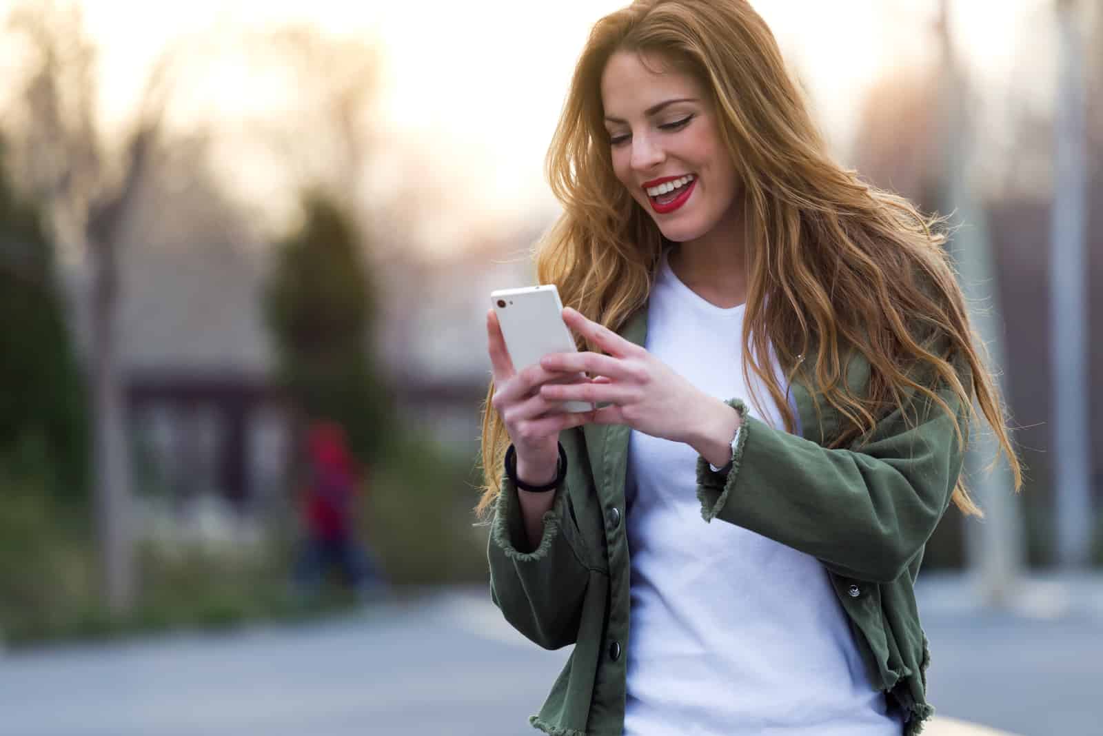 une femme debout dans la rue en riant et en appuyant sur un téléphone